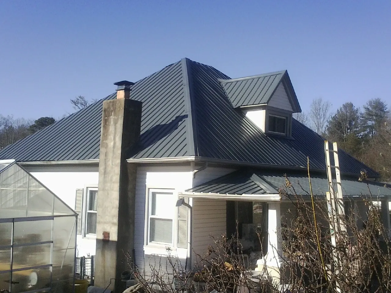Dark blue standing seam metal roof on a white farmhouse with dormer — Slate & Tile Roof Repair by Roofing Brothers in Baker